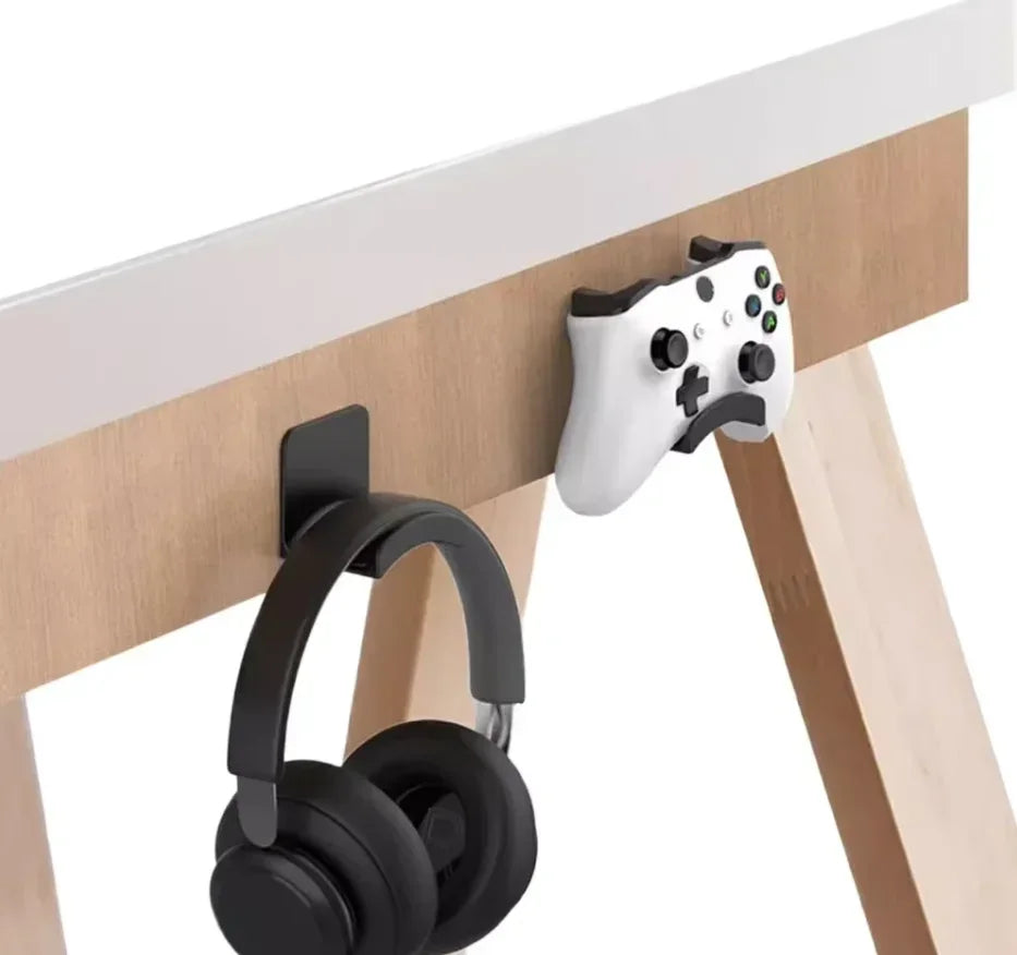 Black adhesive headphone hook holding headphones on a desk side