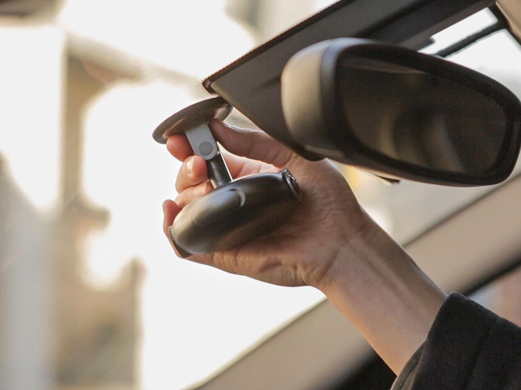 Person adjusting a car side mirror with a blurred background